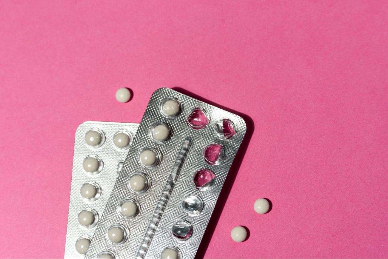 dwa blistry pigułek antykoncepcyjnych na różowym tle